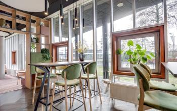 Moderne kantoorruimte huren in kantoorpand Maanlander 47, Amersfoort Calveen. Grote ramen laten veel licht binnen, met groen en hoge tafels in een uitnodigende omgeving.