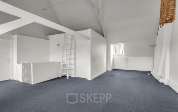 Leeg kantoorpand op Stadsring 248-250 in Amersfoort met grijze vloerbedekking, witte muren en een ladder naar een verhoogde opslagruimte. De ruimte is licht en heeft hoge plafonds.