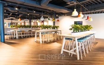 Moderne werkruimte van kantoorpand aan Databankweg 26, Amersfoort De Hoef, met hoge tafels, krukken en groene planten.