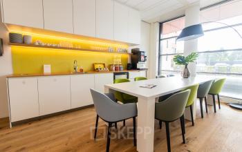 Moderne pantry in kantoorpand op Databankweg 26, Amersfoort De Hoef. Voorzien van keuken, lange tafel en kleurrijke stoelen.