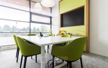 Moderne vergaderruimte in kantoorpand op Databankweg 26, Amersfoort De Hoef, met groene stoelen rond een witte tafel en een krijtbord aan de muur.