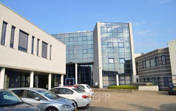 De voorzijde van een modern kantoorpand met glasgevels, gelegen aan de Algolweg 9-11 in Amersfoort De Hoef, met meerdere geparkeerde auto's zichtbaar op de voorgrond.