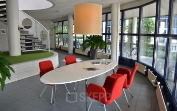 Lichte kantoorruimte met opvallende rode stoelen rond een ovale tafel, gelegen aan de Algolweg 9-11 in Amersfoort De Hoef. Voorzien van een moderne inrichting.
