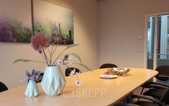 Vergaderruimte in kantoorpand op Algolweg 9-11 in Amersfoort, met moderne kunst aan de muur en decoratieve vazen op tafel. Ideaal voor bedrijven die kantoorruimte willen huren.