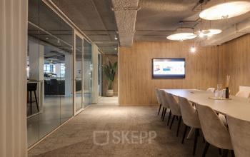 Vergaderruimte in kantoorgebouw op Vanadiumweg 11 in Amersfoort Isselt, met lange tafel, comfortabele stoelen, houten wandafwerking en moderne verlichting. Ideale kantoorruimte huren voor zakelijke bijeenkomsten.