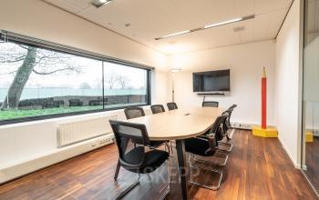 Vergaderruimte in kantoren op Prof. W.H. Keesomlaan 12, Amstelveen, met lange tafel, stoelen, groot raam en een monitor aan de muur. Kantoorruimte huren.