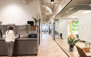 Kantoorruimte huren aan H.J.E. Wenckebachweg 123 in Amsterdam Amstel Business Park met glazen wanden, houten vloer en een persoon bij een koffiezetapparaat.