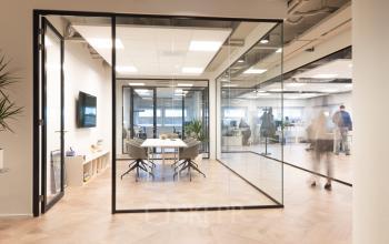 Moderne kantoorruimte huren op H.J.E. Wenckebachweg 123, Amsterdam Amstel Business Park met glazen wanden, vergaderruimte, en werkplekken. Mensen zijn bezig met zakelijke activiteiten.