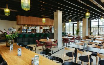 Kantoorruimte huren in Amsterdam Amstel Business Park aan de Joan Muyskenweg 137. Moderne werkplek met houten tafels, design stoelen, en rustige verlichting. Geschikt voor informeel overleg en ontspannen werksessies.