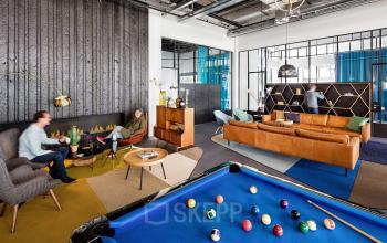 Gezellige gemeubileerde kantoorruimte huren aan Joan Muyskenweg 22, Amsterdam Amstel Business Park, met moderne lounge, pooltafel en verschillende werkplekken. Mensen werken aan bureau en relaxen in loungehoek.