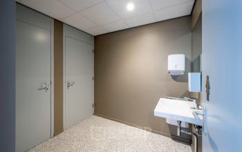 Neutraal ingerichte toiletruimte in kantoorpand gelegen aan Joop Geesinkweg 601, Amsterdam Amstel Business Park. Voorzien van wasbak en neutrale muren, dit biedt een efficiënte aanvulling bij kantoorruimte huren.