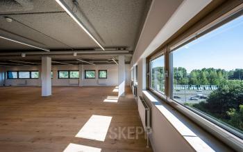Interieur van een leeg kantoorpand op Joop Geesinkweg 501, Amsterdam Amstel Business Park met houten vloeren, grote ramen met uitzicht op groen en veel natuurlijk licht.