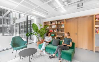 Kantoorruimte huren aan de Mr. Treublaan 7 in Amsterdam Amstel met moderne, gemeubileerde zitruimte. Twee personen zitten op een groene bank, druk in gesprek met laptops op schoot.