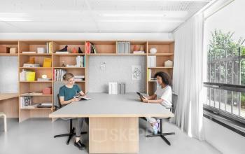 Moderne kantoorruimte huren aan Mr. Treublaan 7, Amsterdam Amstel met grote ramen, boekenplanken, twee vrouwen werkend aan een tafel.