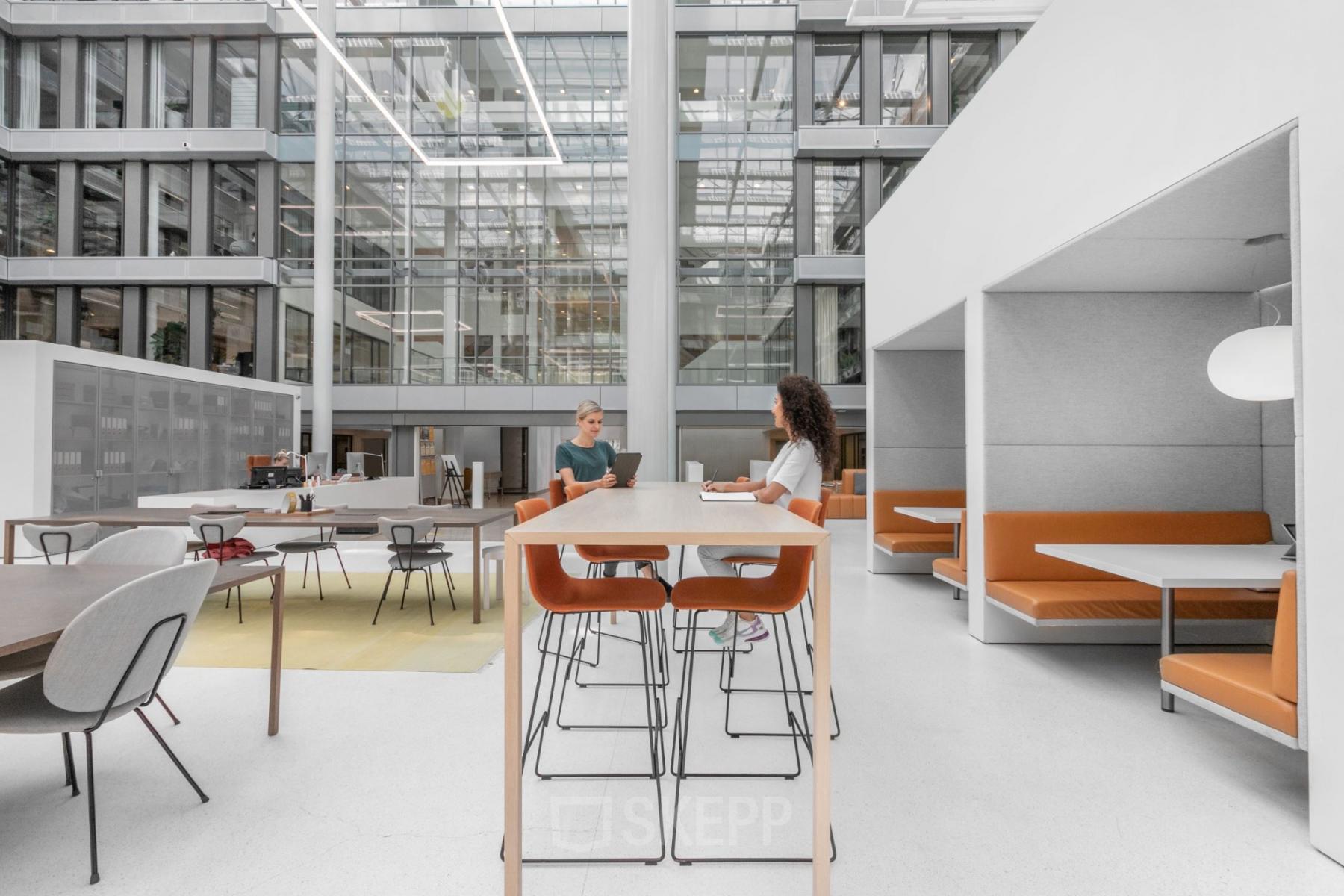 Moderne werkplekken in kantoorpand aan Mr. Treublaan 7, Amsterdam Amstel, met collega's in overleg bij een lange tafel.