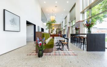 Moderne kantoorruimte met hoge plafonds en veel lichtinval, gelegen aan Willem Fenengastraat 16, Amsterdam Amstel. Ruimte is stijlvol gemeubileerd met banken en hoge tafels, ideaal voor huur als kantoorpand.