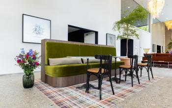 Modern gemeubileerde kantoorruimte in Amsterdam Amstel met groene bank, houten stoelen en een kleurrijk vloerkleed voor flexibel werken.