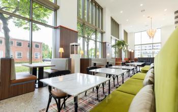 Moderne coworking ruimte huren op Willem Fenengastraat 16 in Amsterdam Amstel met stijlvolle groene en bruine inrichting en grote ramen voor veel natuurlijk licht.