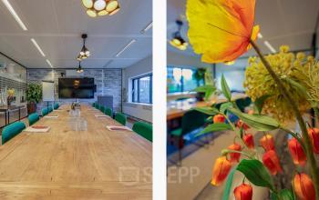 Vergaderruimte in een kantoorpand met lange houten tafel, groene stoelen en bloemen op tafel, gelegen op Prins Bernhardplein 200 in Amsterdam Amstel.