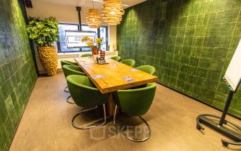 Groene vergaderruimte in Amsterdam Amstel met houten tafel, groene stoelen en planten, ideaal voor kantoorruimte huren.