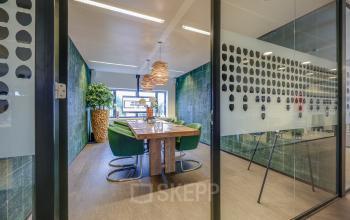 Moderne kantoorruimte met glazen wanden op Prins Bernhardplein 200, Amsterdam Amstel. Houten tafel met groene stoelen, geschikt voor vergaderingen of samenwerking.