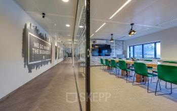 Kantoorruimte huren in Amsterdam Amstel op het Prins Bernhardplein 200. Moderne vergaderruimte met groene stoelen en lange houten tafel, naast een gang met motiverende muurschildering.