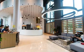 Moderne kantoorruimte huren op Amstelplein 8, Amsterdam Amstel, met stijlvolle receptie en gezellige zithoek. Mensen voeren zakelijke gesprekken en werken op laptops.