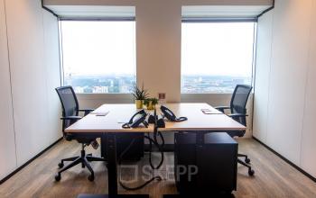 Verlichte kantoorruimte op Amstelplein 8, Amsterdam Amstel met twee bureaus, stoelen en uitzicht over de stad. Deze ruimte is geschikt voor wie een functionele werkplek zoekt.