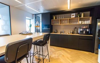 Moderne pantry in een kantoorpand op Amstelplein 8, Amsterdam Amstel, met hoge stoelen en een koffiezetapparaat. Ideaal voor kantoorruimte huren.