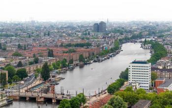 Uitzicht op Amstelplein 8 in Amsterdam Amstel, met de rivier en de stad op de achtergrond. Een kantoorpand is zichtbaar nabij het water.