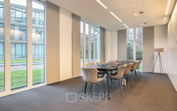 Vergaderruimte in kantoorpand op De Cuserstraat 91, Amsterdam Buitenveldert, met moderne tafel en stoelen, uitzicht op groene buitenruimte.