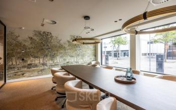 Vergaderruimte in Amsterdam Buitenveldert met lange houten tafel, comfortabele stoelen en moderne verlichting, ideaal voor kantoorruimte huren. Grote ramen bieden veel natuurlijk licht.