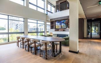 Lichte, moderne kantoorruimte met grote ramen en comfortabele stoelen bij een lange tafel, ideaal voor vergaderingen in het kantoorpand op Zwaansvliet 1, Amsterdam Buitenveldert.