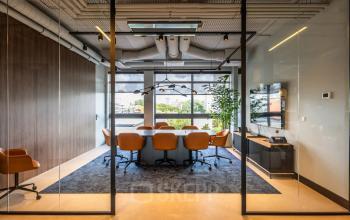 Vergaderruimte in kantoorpand met lange tafel, bruine leren stoelen en groot raam met uitzicht op Amsterdam Buitenveldert. Modern interieur met glazen wanden en houten accenten, geschikt voor kantoorruimte huren.