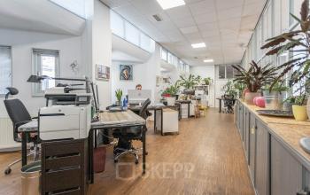 Moderne kantoorruimte met houten vloer op Oudeschans 21 te huren, voorzien van bureaus, planten en kunst aan de muur.