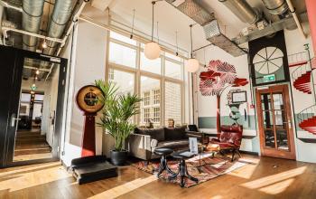 Kantoorruimte huren aan Nieuwezijds Voorburgwal 162, Amsterdam Centrum; gemeubileerd met zitplaatsen, planten en decoraties aan de muur. Een persoon zit op een bank met een laptop, werkend.