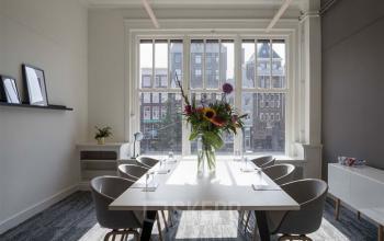 Lichte kantoorruimte op Rokin 92-96, Amsterdam Centrum, met grote ramen, bloemdecoratie op tafel en moderne stoelen. Perfecte plek voor vergaderingen. Huren op centrale locatie.