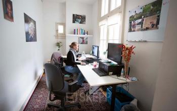 Kantoorpand huren aan Schippersgracht 1-3, Amsterdam Centrum. Persoon werkt op computer in lichte werkruimte met twee bureaus, boekenplank en decoratieve elementen.