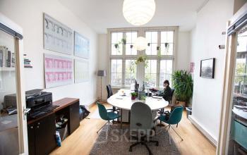 Kantoorruimte huren aan Schippersgracht 1-3 in Amsterdam Centrum, met grote ramen, ronde tafel en bureaustoelen waar een persoon achter een computer werkt.