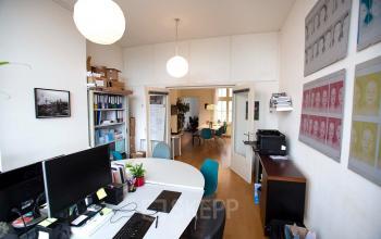 Kantoor te huur op Schippersgracht 1-3 in Amsterdam Centrum, voorzien van een lichte werkruimte met bureaus, stoelen en computers, inclusief een vergaderruimte in de achtergrond.