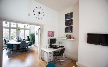 Ruime kantoorruimte huren op Schippersgracht 1-3 in Amsterdam Centrum, met meerdere bureaus, stoelen, een computer en een vergadertafel met stoelen aan de raamzijde.