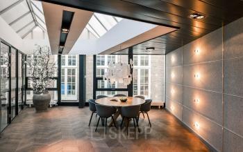 Stijlvol kantoorpand in Amsterdam Centrum op Muiderstraat 1 met moderne verlichting, glazen wanden en houten vloer. Kantoorruimte huren mogelijk in lichte, efficiënte omgeving. Grote planten en design lampen sieren de ruimte.