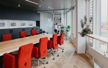 Vergaderzaal in een kantoorpand op Muiderstraat 1, Amsterdam Centrum met een lange tafel en rode stoelen; een persoon is bezig met werkactiviteiten.
