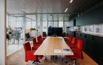 Vergaderruimte met lange tafel, omringd door rode stoelen, in een moderne kantoorruimte op Muiderstraat 1, Amsterdam Centrum. De ruimte heeft glazen wanden en een grote monitor aan de muur.