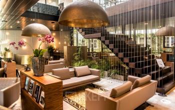 Moderne lounge met luxe zithoeken en grote hanglampen in het kantoorpand op Muiderstraat 1, Amsterdam Centrum. Groen decor en een opvallende trap complementeren de ruimte voor kantoorruimte huren.