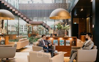 Kantoorpand op Muiderstraat 1 in Amsterdam Centrum met een moderne lounge-inrichting. Twee zakenmensen voeren een gesprek in een stijlvolle zithoek. Ideale locatie voor wie kantoorruimte wil huren.