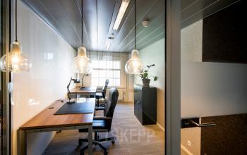 Kantoorruimte op Muiderstraat 1 in Amsterdam Centrum met twee bureaus, stoelen en verlichting; ideaal voor bedrijven die kantoor willen huren. Grote ramen zorgen voor natuurlijk lichtinval.