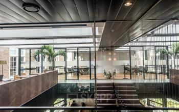 Moderne kantoorruimte te huur in kantoorpand op Muiderstraat 1, Amsterdam Centrum, met glazen wanden, houten vloeren en een open indeling met vergaderruimte en werkplekken.