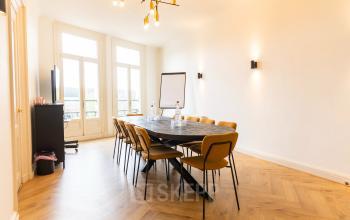 Kantoorpand op Prins Hendrikkade 21 in Amsterdam Centrum met een moderne vergaderruimte, voorzien van een lange tafel, stoelen en een presentatiescherm.