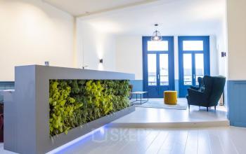 Moderne receptieruimte in kantoorpand aan Prins Hendrikkade 21, Amsterdam. Helder verlicht met plantenwand en comfortabele zitmogelijkheden, ideaal voor bedrijven die kantoorruimte willen huren in het centrum.
